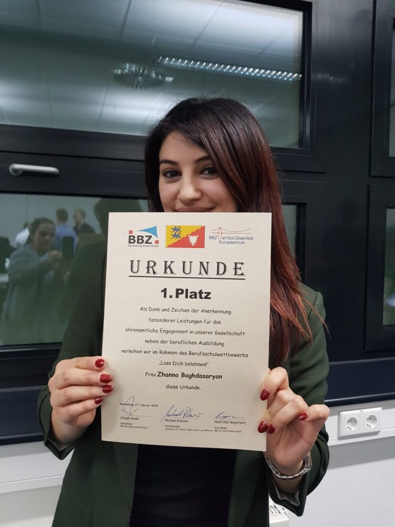 Die Preisverleihung „Lass dich belohnen!“ ist ein jährlicher Berufsschulwettbewerb im Kreis Rendsburg-Eckernförde, der Auszubildende und Fachschüler*innen für ihr ehrenamtliches Engagement würdigt, indem er sie mit Geldpreisen für ihre zeitintensive Arbeit in Vereinen, Feuerwehr, Jugendorganisationen und ähnlichen Bereichen auszeichnet. Zhanna Baghdasaryan, unser damaliges Vorstandsmitglied aus Armenien, hat im Jahr 2020 den ersten Platz erhalten.